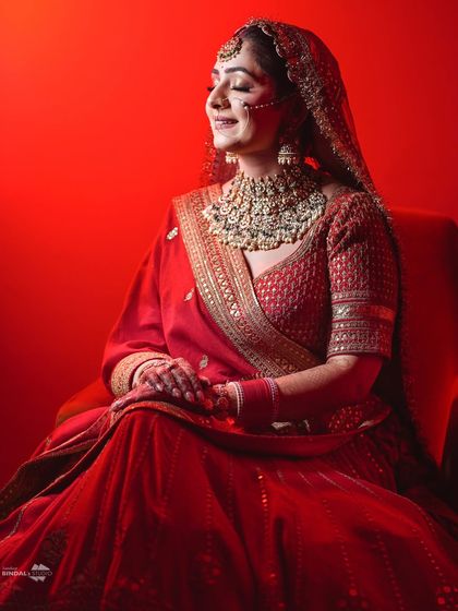 A powerful bridal portrait with a bold red background. The dramatic lighting and her serene expression make this a striking and unforgettable image.