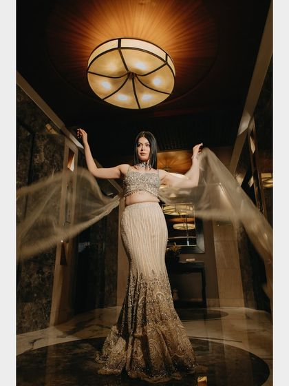 A stunning solo portrait of the bride. The flowing fabric of her gown and the dramatic uplighting create a sense of movement and elegance, highlighting her poise and the beautiful details of her attire.