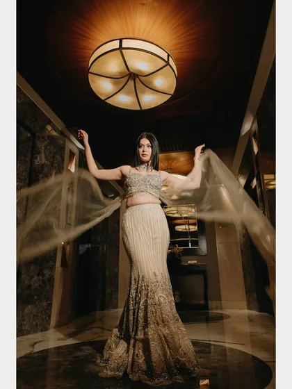 A stunning solo portrait of the bride. The flowing fabric of her gown and the dramatic uplighting create a sense of movement and elegance, highlighting her poise and the beautiful details of her attire.