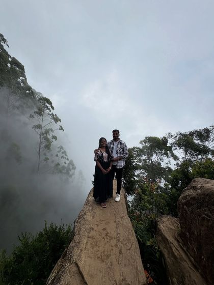 A couple standing on Dolphin's Nose in Kodaikanal, surrounded by mist.