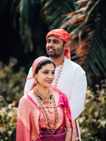 A beautiful portrait of a couple in traditional attire, the bride in pink and the groom in white, standing in a garden.