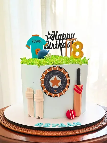 A cricket-themed cake for an 8th birthday, featuring the Indian cricket team logo, a bat, ball, and a personalized jersey.