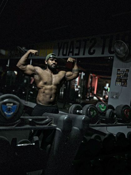 On top. A classic front double bicep pose in a dimly lit gym. The mood is intense.
