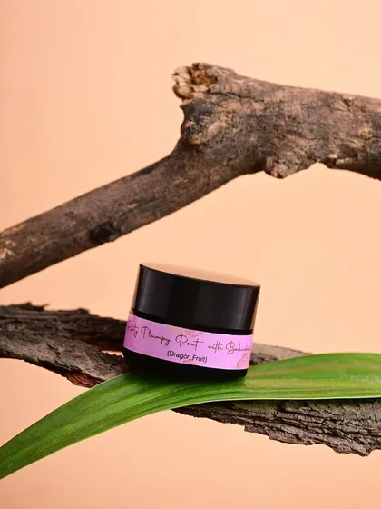 A minimalist composition featuring a lip balm from Pure by Priyanka on a tree branch. This artistic shot creates a natural, organic, and slightly moody feel.