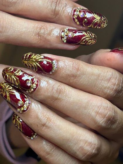 An opulent and festive nail art set. This design features a deep red base with intricate 3D gold leaf patterns and sparkling rhinestone accents.