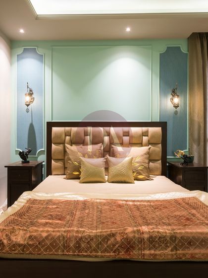 A closer view of the bed, showcasing the intricate, cushioned headboard and the soft, layered bedding. The traditional wall sconces add a warm, ambient glow to the space.