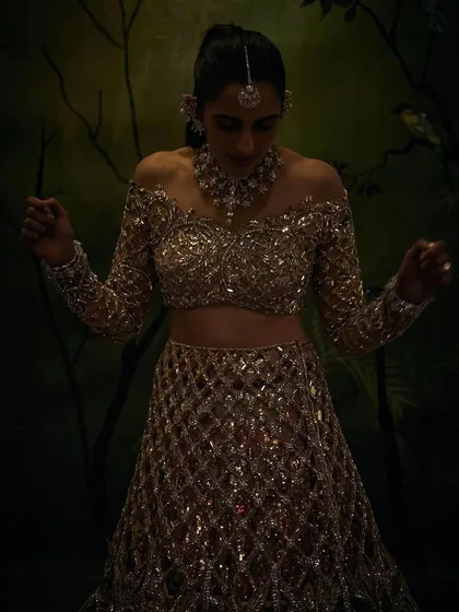 A moody, atmospheric shot of the gold Manish Malhotra lehenga, highlighting its sparkle and dramatic silhouette in low light.