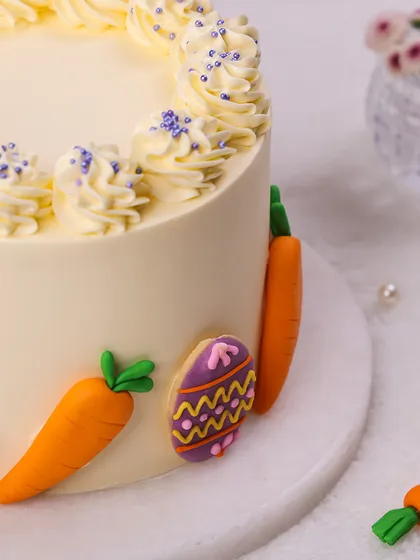 A close-up of our elegant Easter Cake, adorned with beautifully decorated Easter egg cookies and fondant carrots.