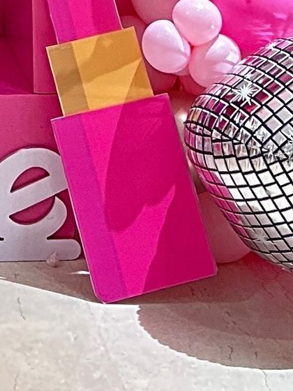 A close-up of a Barbie-themed setup showing a lipstick prop and a silver disco ball balloon, adding to the fun and glamorous vibe.