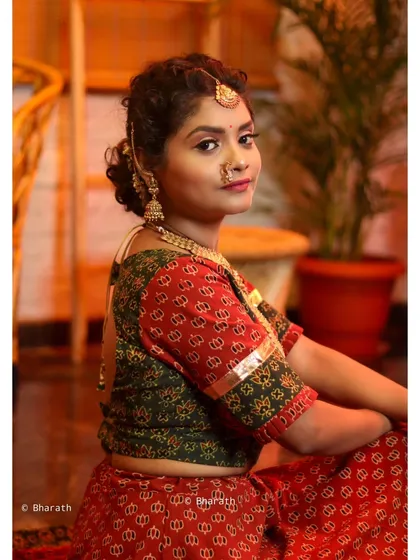 A seated portrait capturing a quiet, reflective moment. The focus is on the model's profile and the intricate details of her ethnic attire.