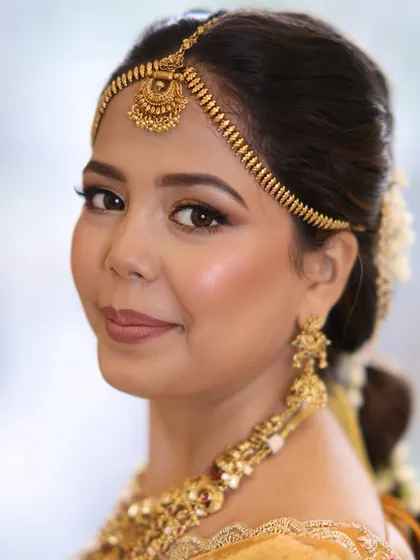 A close-up of the South Indian bride, showing how the neat hairstyle complements her radiant makeup and traditional gold jewelry.