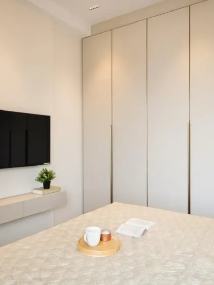 In this bedroom, we placed the television on a floating console table next to the main wardrobe unit. This creates a lighter, more open feel while still maintaining a cohesive look with matching finishes and long, elegant handles.