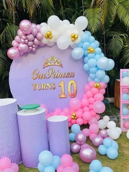 A pretty princess theme for a 10th birthday. This outdoor setup features a custom backdrop and a pastel pink, blue, and purple balloon arch.