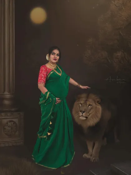 In this moody, painterly portrait, a mother-to-be stands beside a lion under a full moon. The deep green saree and dramatic lighting evoke a sense of mystery and ancient power, transforming a maternity photo into a mythological narrative.