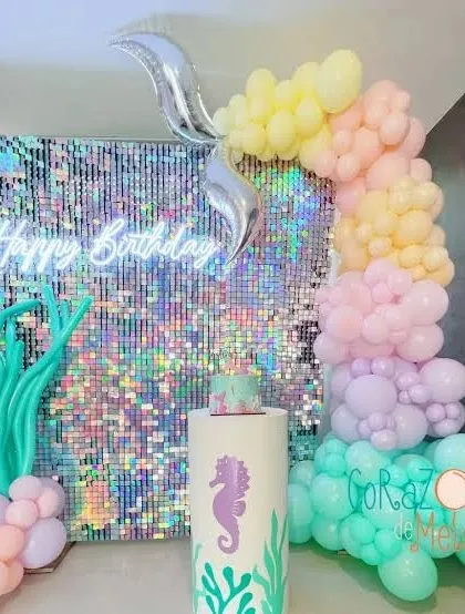 A mermaid-themed birthday with an iridescent shimmer wall, a 'Happy Birthday' neon sign, and a pastel balloon garland.