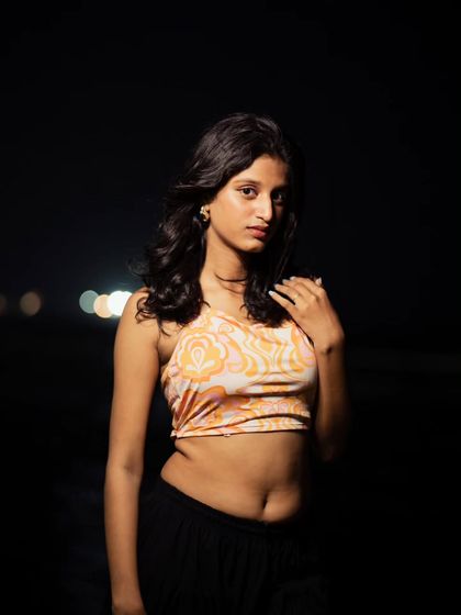 A direct and engaging portrait from the same beach shoot. The lighting is focused on the subject, making her stand out against the dark, minimalist background.