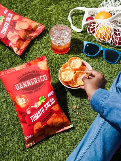 A relaxed picnic scene with Banner & Co Tomato Salsa chips. The overhead shot captures a perfect summer day, associating the brand with leisure and outdoor enjoyment.