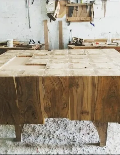 This custom center table, made from blocks of solid teak wood, is seen here mid-process. The varied grain of the wood blocks creates a rich, patchwork-like surface.