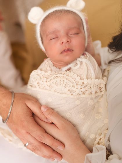 A close-up of a newborn wearing a cute bear bonnet, held securely in her parents' hands.