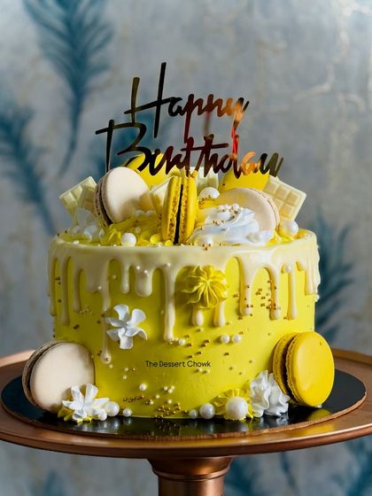 A sunny and cheerful custom tall cake in yellow, decorated with a white chocolate drip and macarons. A perfect way to brighten up any birthday celebration.