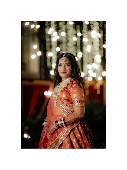 A stunning portrait of a bride in her orange and red lehenga, set against a backdrop of twinkling lights. A classic and beautiful bridal shot.