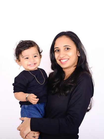 A bright and happy portrait of a mother and her smiling baby. Their coordinated black outfits and the simple white background make their joyful connection the star of the show.