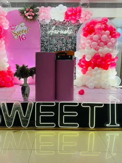 A "Sweet 16" birthday stage decoration in pink and white, featuring a balloon-filled arch, a sequin panel, and a large "SWEET 16" light-up sign.