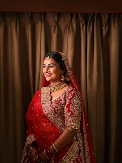A radiant smile from a bride in her classic red lehenga, her makeup looking fresh and luminous.