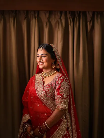 A radiant smile from a bride in her classic red lehenga, her makeup looking fresh and luminous.