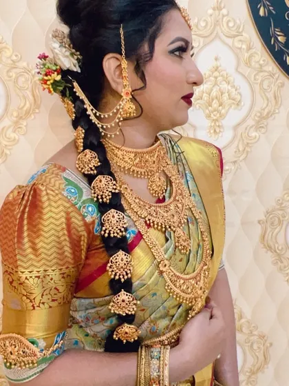 A traditional South Indian bridal look. The focus is on the elaborate temple jewelry adorning the long, thick braid, and the classic makeup with defined eyes and a deep red lipstick.
