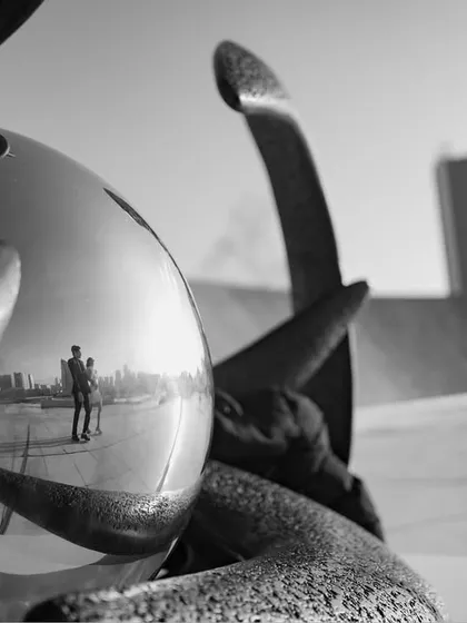 An abstract and artistic black and white shot. The reflection of the photographer and the Baku landscape in a metallic sphere creates a unique, meta-photograph that is visually intriguing.