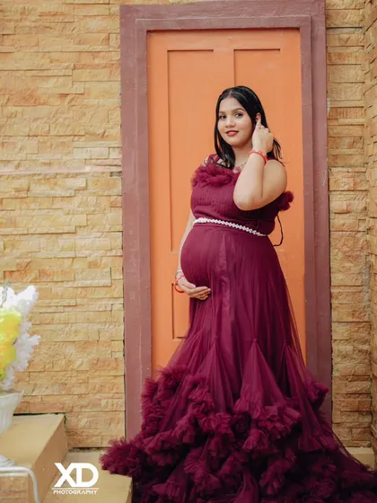 A confident solo portrait of the mother-to-be in a maroon gown, posing on a rustic staircase.