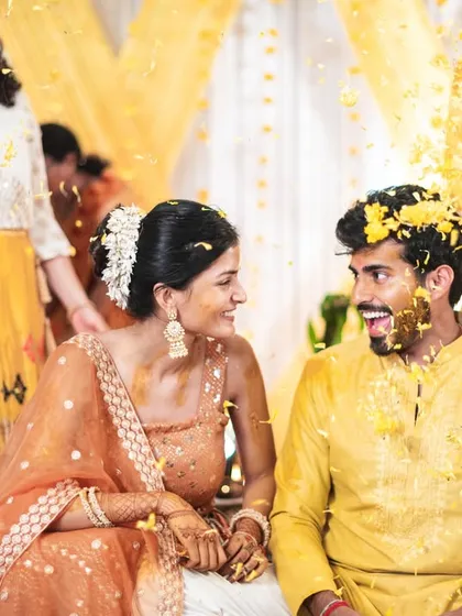 A shower of marigold petals during the haldi. The couple's expressions are a mix of surprise and delight.
