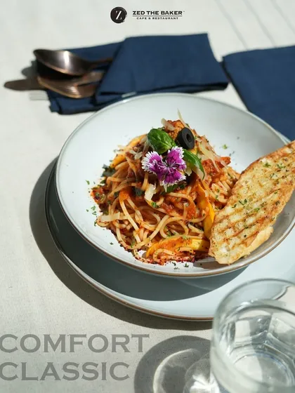 My take on a comfort classic. This is my tangy arrabbiata spaghetti, tossed with fresh vegetables, garnished with an edible flower, and served with a slice of perfectly grilled garlic bread. It’s a simple dish, elevated.