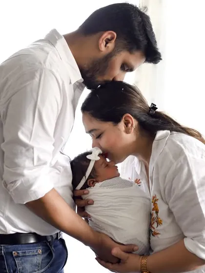 The first family portrait is always so special. Here, both parents share a gentle kiss with their newborn, creating a beautiful memory of their first days together, all dressed in classic, simple white.