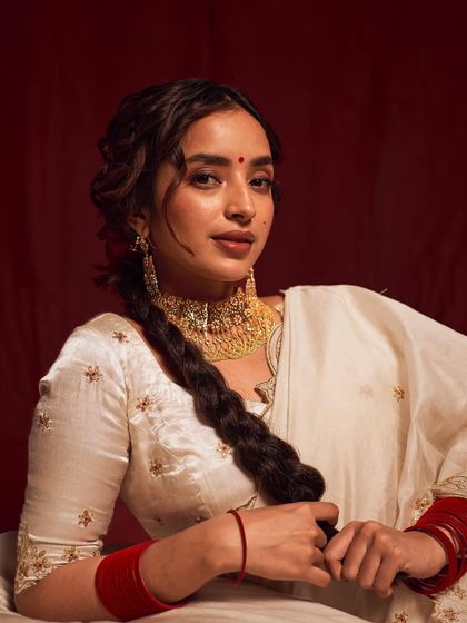 A graceful pose that highlights the traditional red bangles and the embroidered blouse. The model's gentle hold on her braid adds a classic, feminine touch.