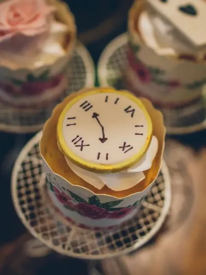A close-up of a whimsical cupcake topped with a fondant clock, capturing the "I'm late!" essence of the White Rabbit. Every dessert is a tiny, edible piece of the story.