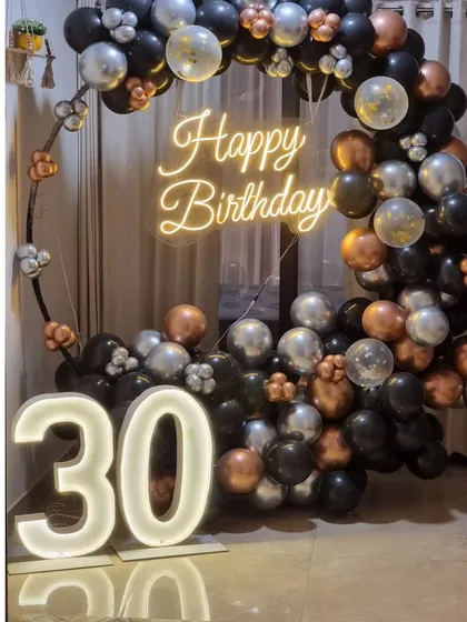 A stylish 30th birthday ring setup with black, silver, and bronze chrome balloons, a neon sign, and large marquee numbers.