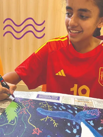 The final touches are often the most fun! This student is using a paint marker to add fine details and outlines to her cosmic whale painting, a technique that helps make the colors pop and adds a professional finish.