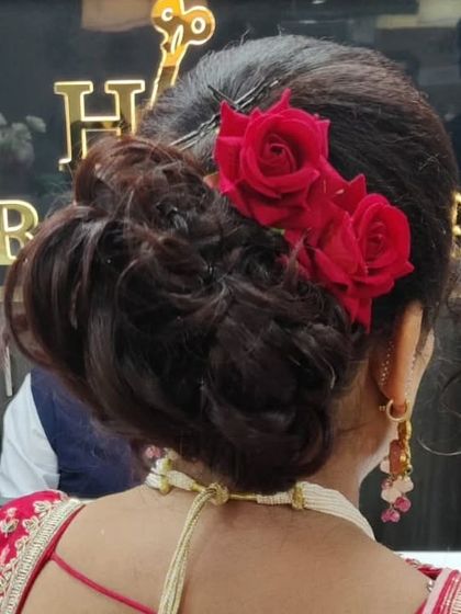 A detailed look at a classic messy bun updo, adorned with three beautiful red roses. This is a popular and timeless choice for weddings and parties.