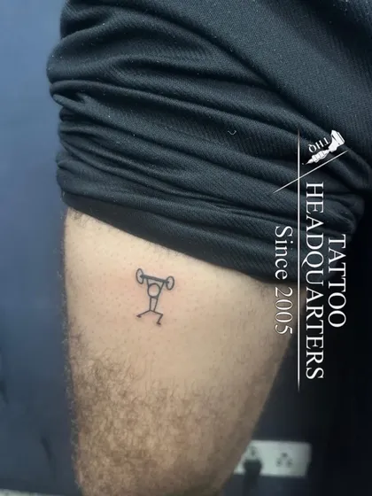 A stick figure lifting a barbell, a fun and minimalist tattoo for a fitness enthusiast.
