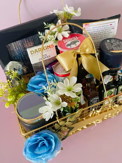 A metal basket hamper for him, curated with miniature liquor bottles, snacks, and chocolates, and decorated with blue flowers.