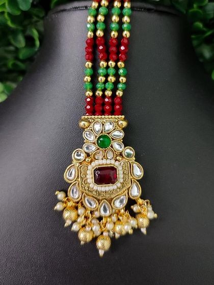 A colorful beaded maang tikka with a kundan pendant featuring red and green stones.