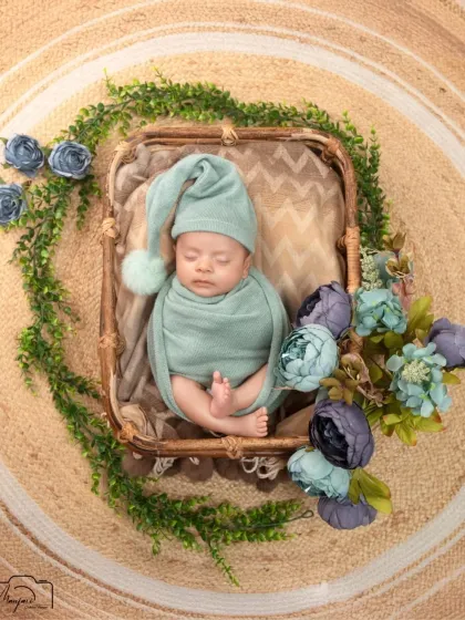 A top-down view of the newborn in the basket, surrounded by a wreath of greenery and flowers. A beautiful, artistic composition.