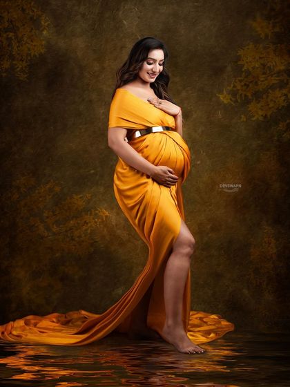 A gentle and contemplative pose in a flowing mustard gown. The dark, moody background and soft lighting create an intimate and artistic fine art maternity portrait.