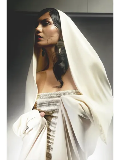 A close-up portrait of the hooded look. The styling of the hood frames the model's face beautifully, while the lighting creates a soft, ethereal glow.