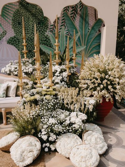 A beautiful photo corner featuring a custom-painted backdrop, lush white florals, and traditional brass lamps, perfectly blending artistry with tradition.