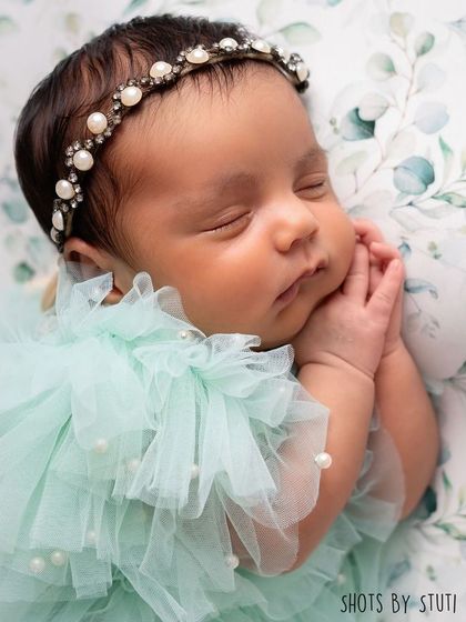 A close-up of the baby in the mint green dress, showing the delicate pearl headband and her peaceful expression.
