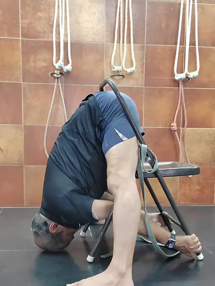 A deep forward fold, Parsvottanasana, using a chair for support. This allows the practitioner to focus on lengthening the spine and stretching the hamstring of the front leg.