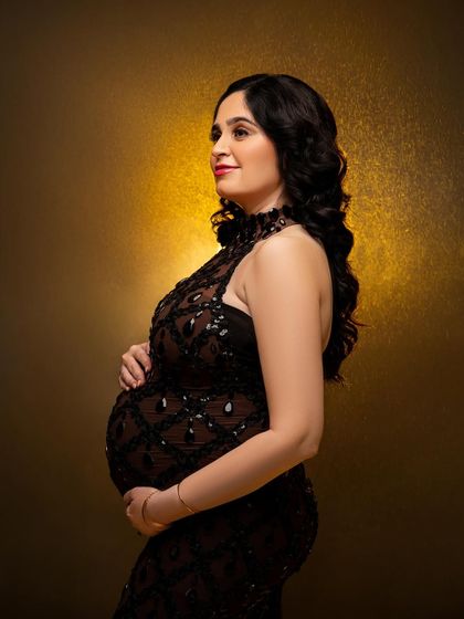 A profile view in the black sequined gown against a warm, golden backdrop. This classic pose highlights the baby bump with elegance and sophistication.
